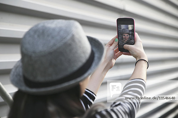 Rückansicht einer jungen Frau  die einen Selfie mit Smartphone nimmt.