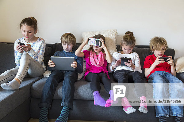 Group picture of five children sitting on one couch using different digital devices
