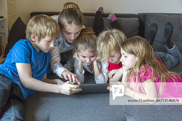 Five children on a couch using digital tablet together