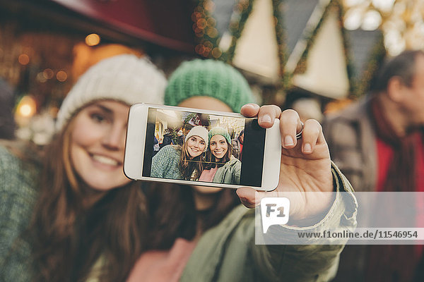 Zwei glückliche Frauen mit einem Selfie auf dem Weihnachtsmarkt