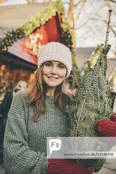 Lächelnde Frau mit eingewickeltem Baum auf dem Weihnachtsmarkt