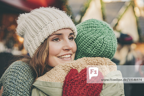 Glückliche Frau umarmt einen Freund auf dem Weihnachtsmarkt