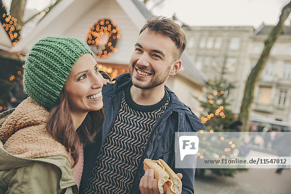 Glückliches Paar beim Snack auf dem Weihnachtsmarkt