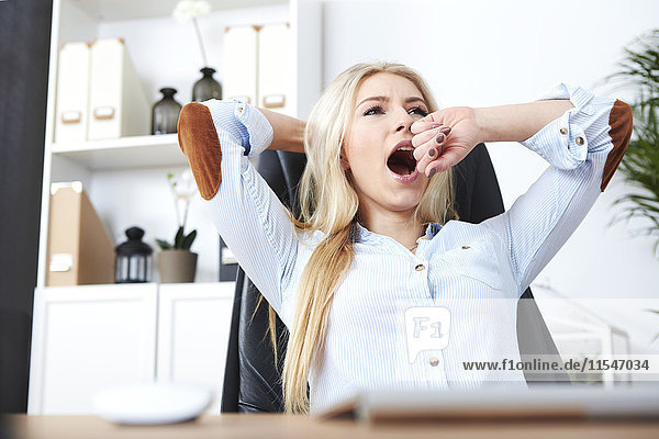 Portrait of blond woman yawning at her desk