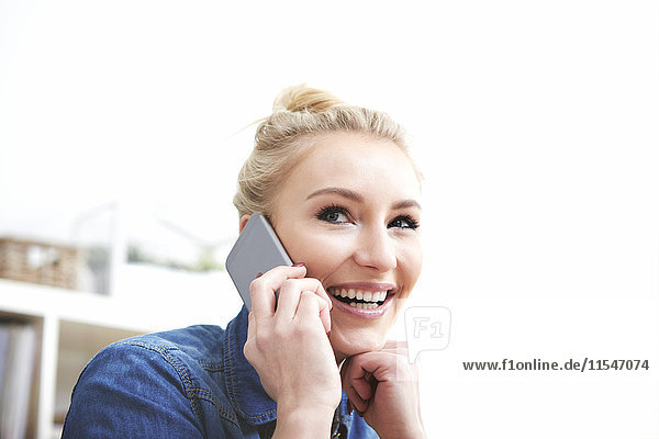 Porträt einer lächelnden blonden Frau beim Telefonieren mit dem Smartphone