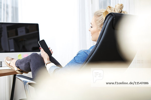 Blond woman sitting at desk with her smartphone listening music