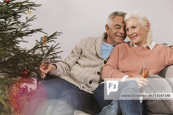 Seniorenpaar sitzt am Weihnachtsbaum und trinkt Champagner.
