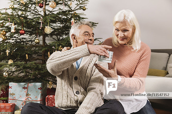 Seniorenpaar tauscht Weihnachtsgeschenke vor dem Baum aus