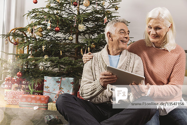 Senior couple looking at a tablet computer in front of Christmas tree