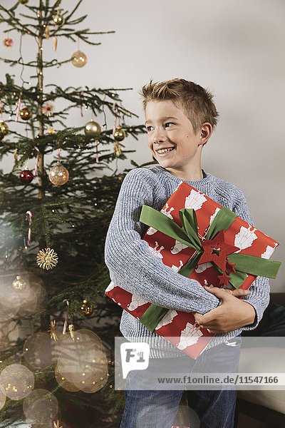 Junge mit einem großen Weihnachtsgeschenk vor dem Baum