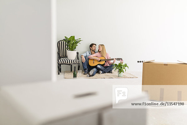 Ein glückliches Paar  das auf dem Boden seines neuen Heims sitzt  Gitarre spielt und zusammen singt.