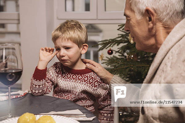 Grandfather comforting sad boy during Christmas dinner