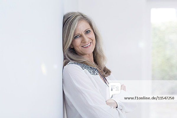 Portrait of smiling blond woman leaning against wall at her new home
