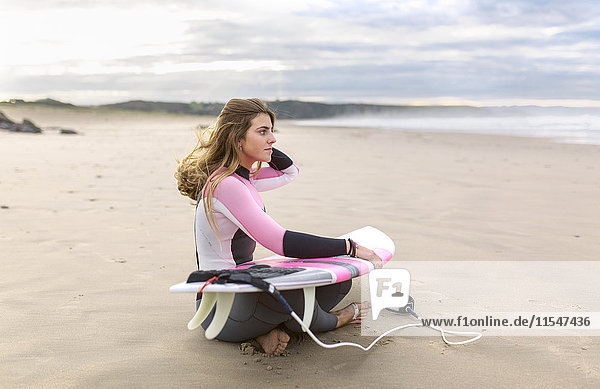 Young surfer woman sitting on the beach