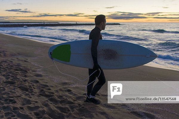 Surfer mit seinem Brett am Strand bei Sonnenaufgang