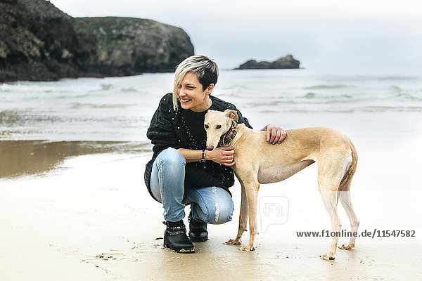 Spanien  Llanes  glückliche junge Frau mit ihrem Windhund am Strand