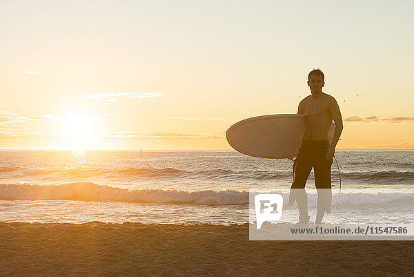 Surfer bei Sonnenaufgang am Strand stehend