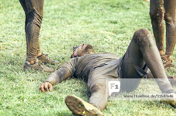 Teilnehmer am extremen Hindernisrennen erschöpft auf Rasen liegend