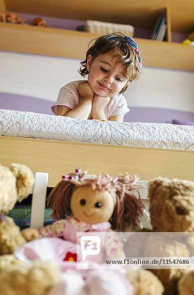 Porträt eines kleinen Mädchens  das auf dem Bett liegt und sein Spielzeug im Vordergrund betrachtet.