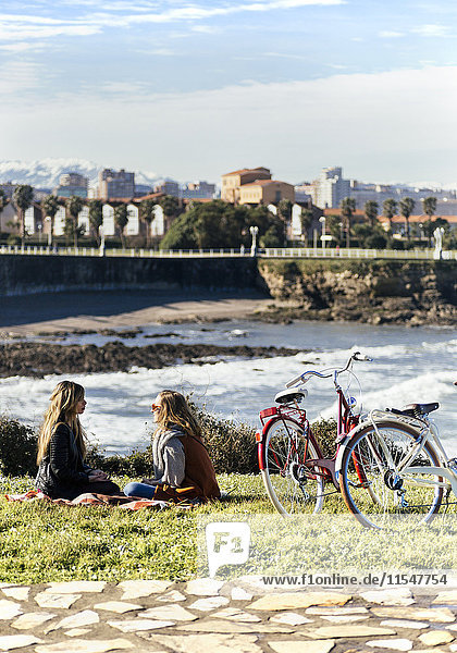 Zwei junge Frauen sitzen mit ihren Fahrrädern am Meer.