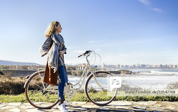 Spanien  Gijon  lächelnde junge Frau auf dem Fahrrad an der Küste