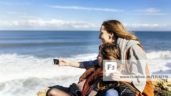 Spain  Gijon  two young women having fun with a smartphone near the sea