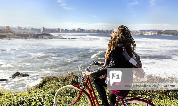 Spain  Gijon  playful young woman riding bicycle at the coast
