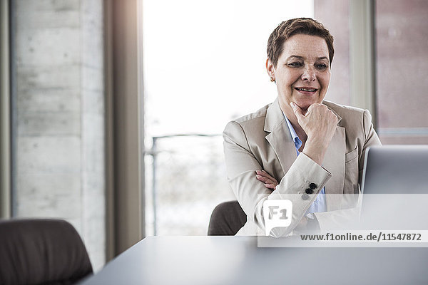 Lächelnde Geschäftsfrau am Schreibtisch mit Blick auf den Laptop