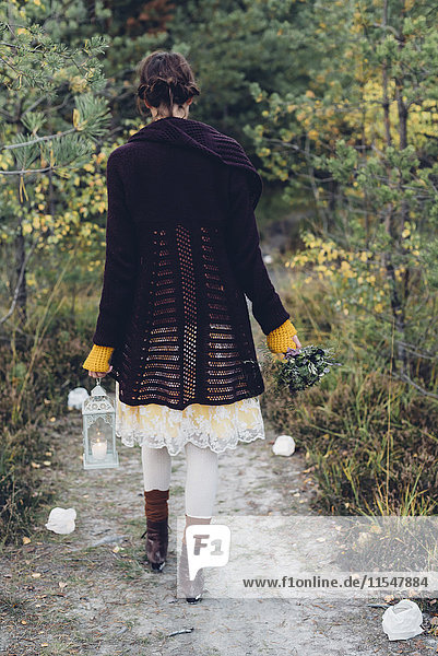 Back view of old-fashioned styled woman with storm lamp walking on a path