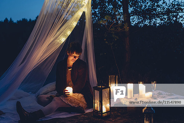 Glückliche Frau in einem romantischen Camp in herbstlicher Natur bei Kerzenschein