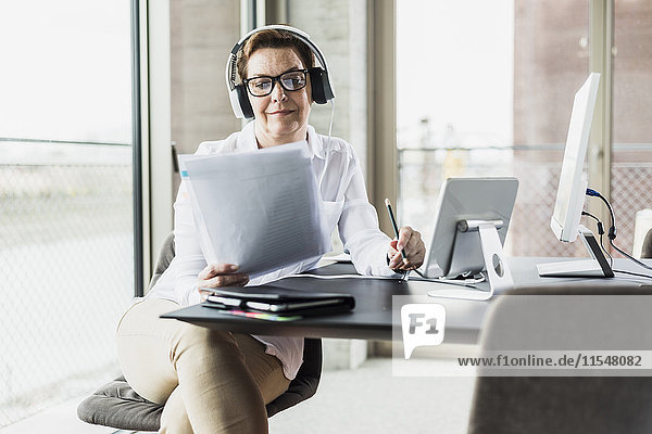 Geschäftsfrau mit Kopfhörer beim Lesen von Dokumenten im Büro