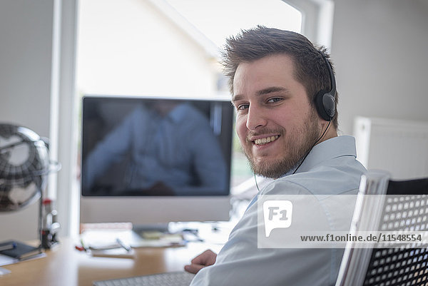Portrait of smiling young man at desk in office wearing headphones