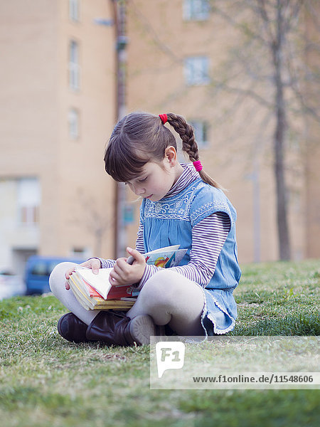 Kleines Mädchen sitzt auf einer Wiese und liest ein Buch.