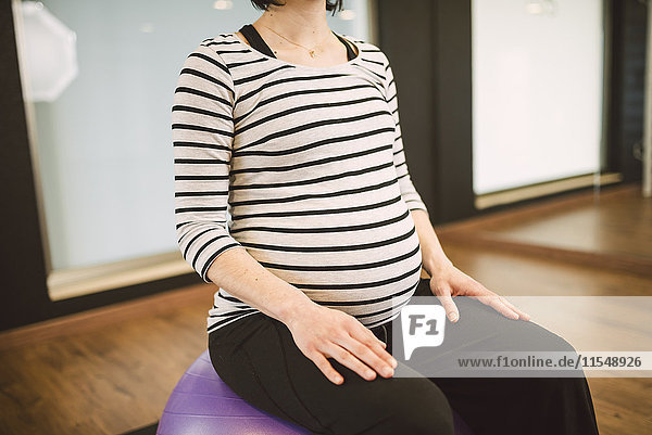Schwangere Frau bei Pilates-Übungen mit Gymnastikball in der Turnhalle