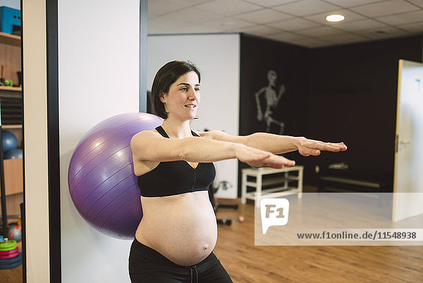 Schwangere Frau bei Pilates-Übungen mit Gymnastikball in der Turnhalle