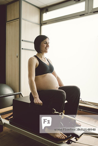 Schwangere Frau  die Pilates-Übungen mit einer Reformer-Pilates-Maschine macht.