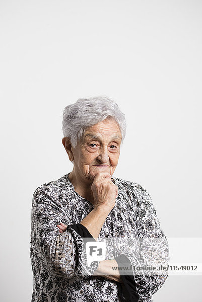 Porträt der lächelnden Seniorin mit Hand am Kinn vor weißem Hintergrund