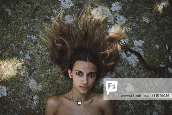 Porträt einer Frau  die auf einem Felsen mit zerzaustem Haar liegt.