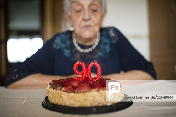 Porträt einer älteren Frau  die die Kerzen auf ihrem Geburtstagskuchen ausbläst.