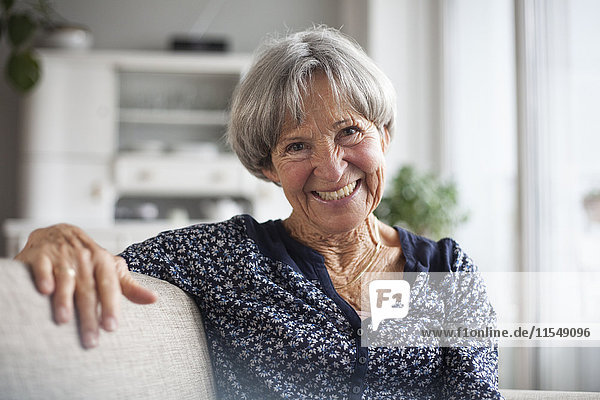Porträt einer glücklichen Seniorin  die zu Hause auf der Couch sitzt.