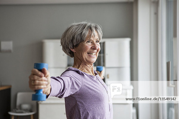 Portrait of happy senior woman doing fitness exercise with dumbbells at home
