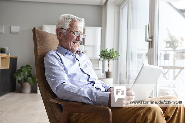 Portrait of senior man sitting on armchair at home using laptop