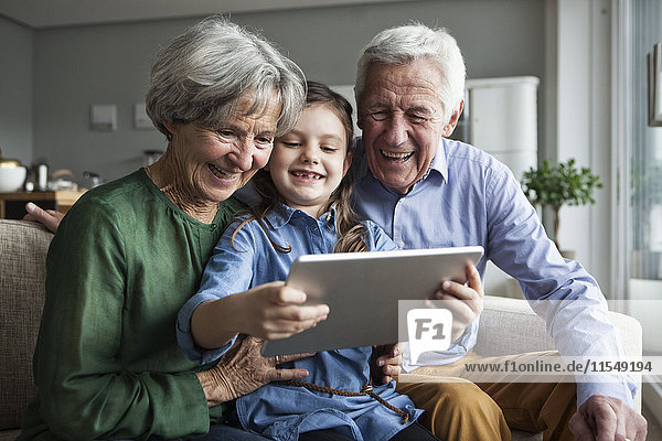 Grandparents and their granddaughter sitting together on the couch looking at digital tablet