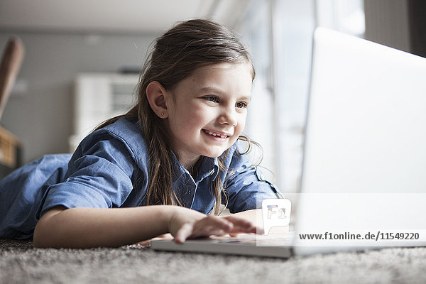 Porträt eines lächelnden kleinen Mädchens auf dem Boden liegend mit Laptop