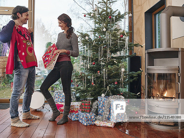 Paar steht vor dem Weihnachtsbaum und packt den Weihnachtspullover aus.