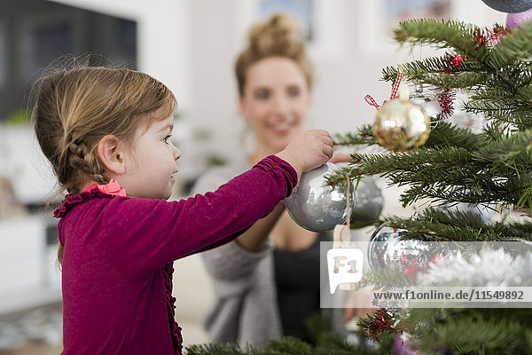 Kleines Mädchen schmückt Weihnachtsbaum mit ihrer Mutter im Wohnzimmer