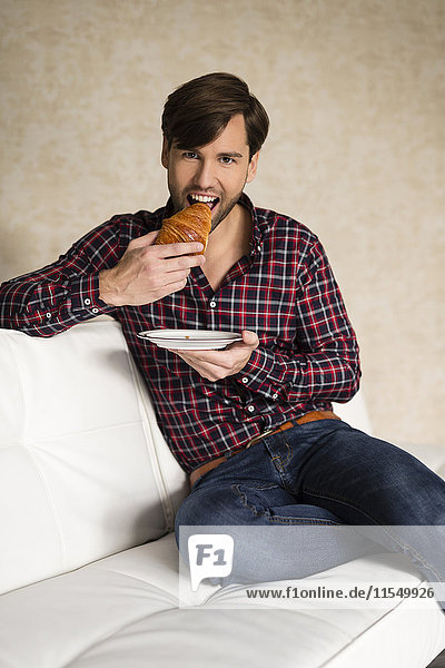 Portrait of man sitting on couch eating a croissant
