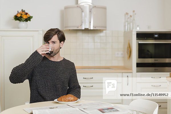 Mann sitzt am Frühstückstisch in der Küche und trinkt Kaffee.