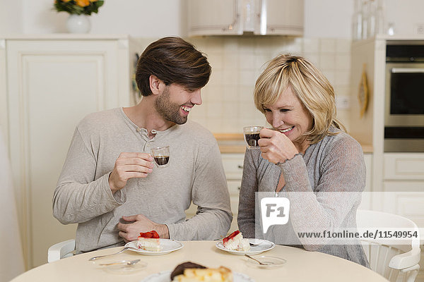 Mutter und erwachsener Sohn trinken Espresso in der Küche und haben Spaß zusammen.