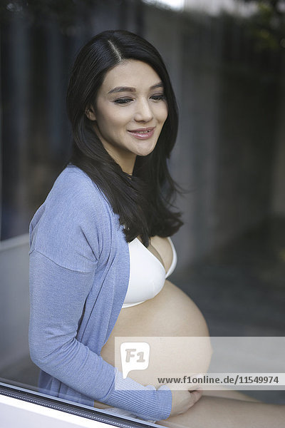 Lächelnde schwangere Frau sitzt hinter der Fensterscheibe